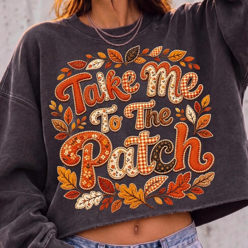 May include: A charcoal gray cropped sweatshirt featuring the text Take Me To The Patch in large, stylized letters. The lettering is filled with various orange, brown, and white patterns, surrounded by a wreath of colorful autumn leaves.