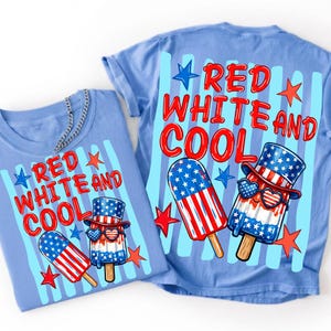 May include: A light blue t-shirt featuring a graphic print with the text RED WHITE AND COOL in red letters. The design includes two patriotic popsicles, one wearing a top hat and heart-shaped sunglasses, surrounded by red and blue stars.