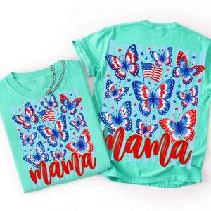 May include: Two mint green t-shirts featuring a graphic print of red, white, and blue butterflies, small American flags, and stars. The word "mama" is printed in a large, red, cursive script font across the bottom of the butterfly design.