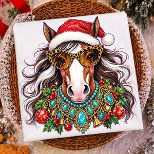 May include: A white t-shirt featuring a colorful illustration of a horse wearing a red Santa hat, leopard print glasses, and a decorative necklace made of turquoise stones, gold bells, red Christmas ornaments, and green holly leaves.