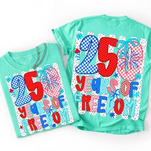 May include: Two mint green t-shirts featuring a graphic design with the text 250 YEARS OF FREEDOM. The design includes large numbers in red and blue checkered and polka dot patterns, firework illustrations, and light blue bows on a striped background.