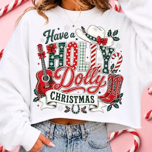May include: A white long-sleeve sweatshirt featuring a graphic print with the text Have a HOLLY Dolly CHRISTMAS. The design includes a white cowboy hat, a red acoustic guitar, red cowboy boots, a candy cane, holly leaves, and a horseshoe.