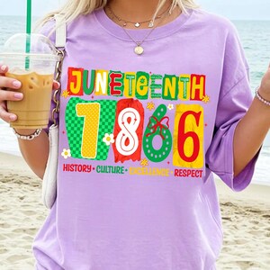 May include: A light purple t-shirt featuring a colorful graphic with the text JUNETEENTH 1865. The design includes the words HISTORY, CULTURE, EXCELLENCE, and RESPECT in red, green, and yellow, with decorative floral and ribbon accents.