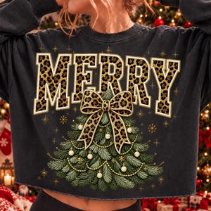 Op de afbeelding: Een antracietgrijs sweatshirt met lange mouwen en het woord MERRY in grote blokletters met een luipaardprint. Onder de tekst staat een afbeelding van een groene kerstboom versierd met gouden kralen en een grote strik met luipaardprint.