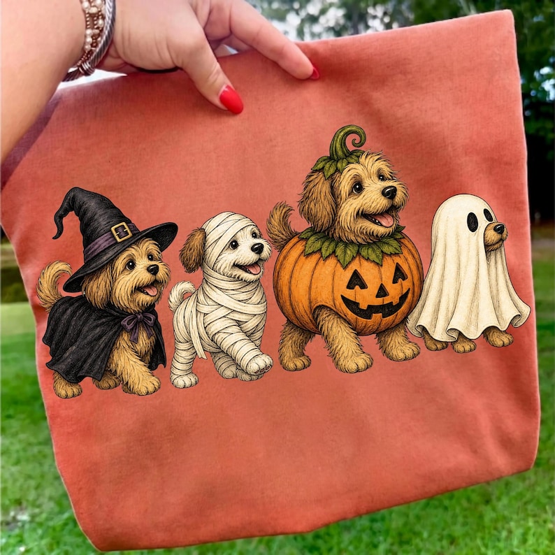 Puede incluir: Un bolso de tela color terracota con un estampado gr&aacute;fico de cuatro perros peque&ntilde;os con disfraces de Halloween. Un perro lleva un sombrero de bruja y una capa negra, otro est&aacute; envuelto en vendas de momia blancas, otro lleva un disfraz de calabaza.