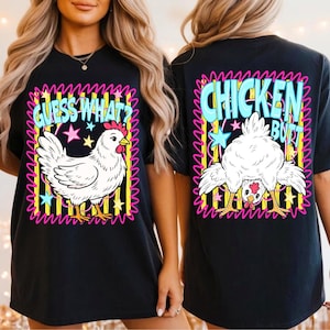 Op de afbeelding: Een zwart t-shirt met een grafische print op de voor- en achterkant. De voorkant toont een witte kip met de tekst "GUESS WHAT?" in het blauw. De achterkant toont een kip die voorover buigt met de tekst "CHICKEN BUTT" in het blauw, omringd door gele strepen, roze krabbels en kleurrijke sterren.
