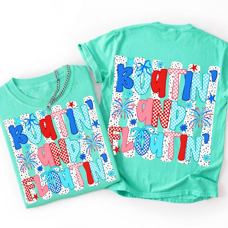 Op de afbeelding: Twee mintgroene t-shirts met een grafische print met de tekst "BOATIN' AND FLOATIN'" in rode, blauwe en roze ruitpatronen. Het ontwerp bevat kleine vuurwerkillustraties, sterren en bloemen op een witte achtergrond met stippen.
