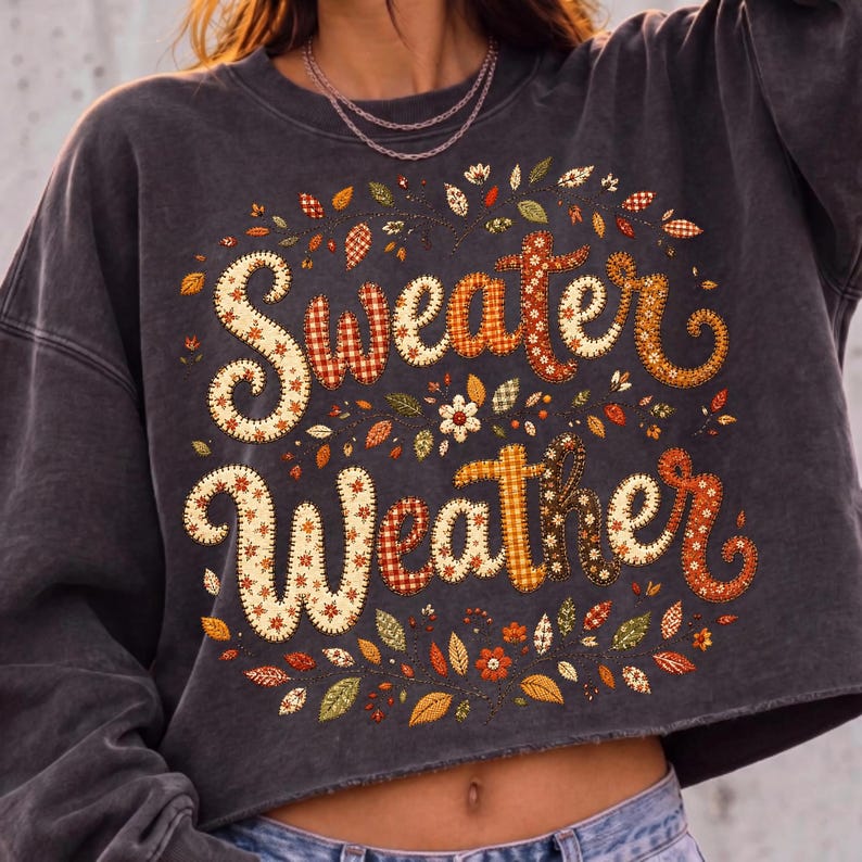 Pu&ograve; includere: Una felpa corta color grigio antracite con la scritta "Sweater Weather" in un carattere decorativo a motivi vari. Le lettere sono riempite con diverse stampe a tema autunnale, circondate da piccole illustrazioni di foglie e fiori colorati.