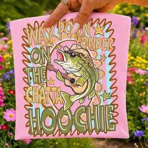 May include: Pink t-shirt with a graphic of a bass wearing a cowboy hat and sunglasses, playing a guitar. The shirt has text that reads "Way Down Yonder On The Chatta Hoochie."