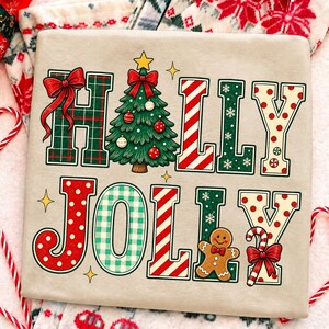 Peut inclure: Un t-shirt beige clair avec le texte Holly Jolly en grandes lettres d&eacute;coratives. Le H est &agrave; carreaux verts avec un n&oelig;ud rouge, le O est un sapin de No&euml;l, les L sont &agrave; rayures rouges et blanches, et le Y est cr&egrave;me &agrave; pois rouges. Le J est rouge &agrave; pois blancs, le O est &agrave; vichy vert, le L est &agrave; rayures rouges et blanches, le L est vert avec des flocons, et le Y est cr&egrave;me &agrave; pois rouges, avec un bonhomme en pain d'&eacute;pice et un sucre d'orge.