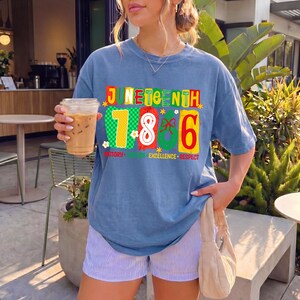 May include: A blue short-sleeve t-shirt featuring a graphic print that reads JUNETEENTH 1866 with the words HISTORY, CULTURE, EXCELLENCE, RESPECT below. The design includes colorful numbers and patterns in red, yellow, and green on the front.