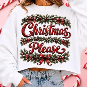 May include: A white cropped sweatshirt featuring a graphic print of green pine branches, red berries, and red bows. The text "Christmas Please" is written in a bold, red, cursive font across the center, framed by the festive holiday greenery.