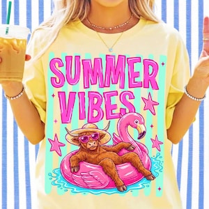 Pu&ograve; includere: Una t-shirt giallo pallido con una stampa grafica di una mucca highland marrone che indossa occhiali da sole rosa e un cappello di paglia, sdraiata su un salvagente a forma di fenicottero rosa. Il testo "SUMMER VIBES" &egrave; stampato in grandi lettere rosa.