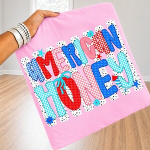 May include: A square pink fabric item featuring the text AMERICAN HONEY in large, multi-colored, patterned letters. The design includes red, blue, and light blue polka dot and checkered patterns, accented with small star and flower graphics.