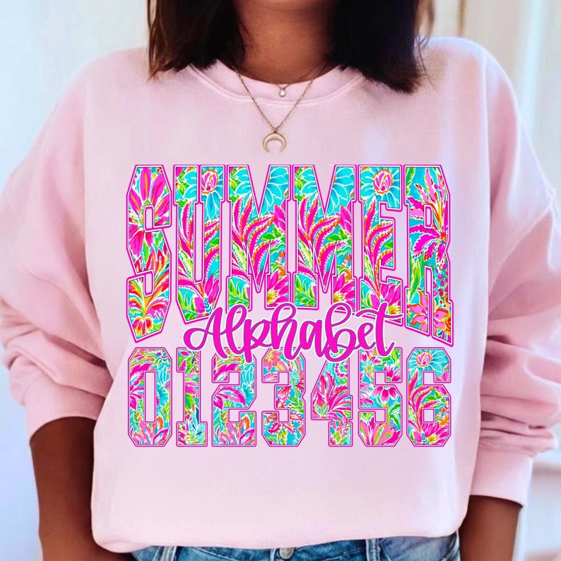 K&ouml;nnte beinhalten: Ein hellrosa Sweatshirt mit dem Wort "SUMMER" in gro&szlig;en, farbenfrohen Blumenbuchstaben. Darunter steht das Wort "Alphabet" in Schreibschrift, gefolgt von den Zahlen 0-6, ebenfalls in einem floralen Design. Das Sweatshirt ist ein l&auml;ssiger Stil.