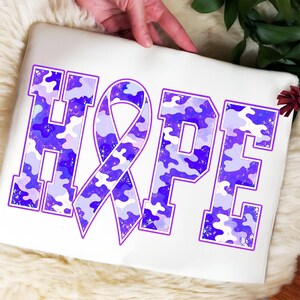May include: A white rectangular pouch featuring the word HOPE in large block letters. The letter O is replaced by an awareness ribbon. The letters and ribbon have a purple and light purple camouflage pattern with small white speckles throughout.