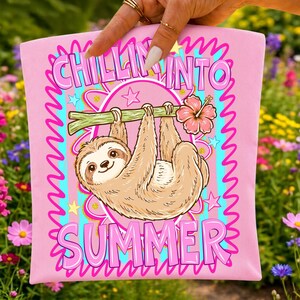 May include: A light pink fabric item featuring a cartoon sloth hanging from a green branch with a pink hibiscus flower. The design includes the text "CHILLIN INTO SUMMER" in bold pink letters, surrounded by blue stripes, pink stars, and squiggly lines.