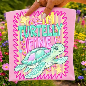 K&ouml;nnte beinhalten: Ein hellrosa Stoffartikel mit einer Grafik einer hellgr&uuml;nen Meeresschildkr&ouml;te. Der Text lautet I'M TURTELLY FINE in gro&szlig;en t&uuml;rkisfarbenen und rosa Buchstaben. Das Design enth&auml;lt gelbe Sterne, einen rosa gewellten Rand und gelbe Streifen.
