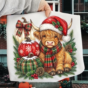 May include: A white fabric surface featuring a graphic illustration of a fluffy Highland cow wearing a red Santa hat and a red and green plaid scarf, surrounded by three pumpkins with plaid patterns, pine branches, pinecones, and holly berries.