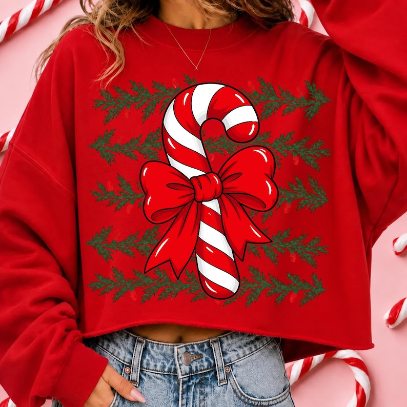 May include: A red long-sleeve sweatshirt featuring a central graphic of a candy cane with a large red bow. The background of the design consists of horizontal rows of green pine branch patterns. The sweatshirt has a crew neckline and a cropped hem.