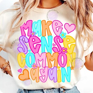 May include: Cream-colored t-shirt with the phrase "MAKE SENSE COMMON AGAIN" in colorful, bubble letters. The design includes hearts and flowers in shades of pink, orange, yellow, and blue.