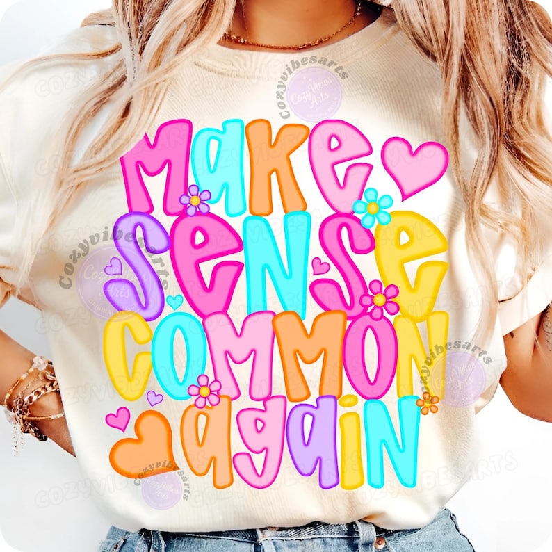 May include: Cream-colored t-shirt with the phrase "MAKE SENSE COMMON AGAIN" in colorful, bubble letters. The design includes hearts and flowers in shades of pink, orange, yellow, and blue.
