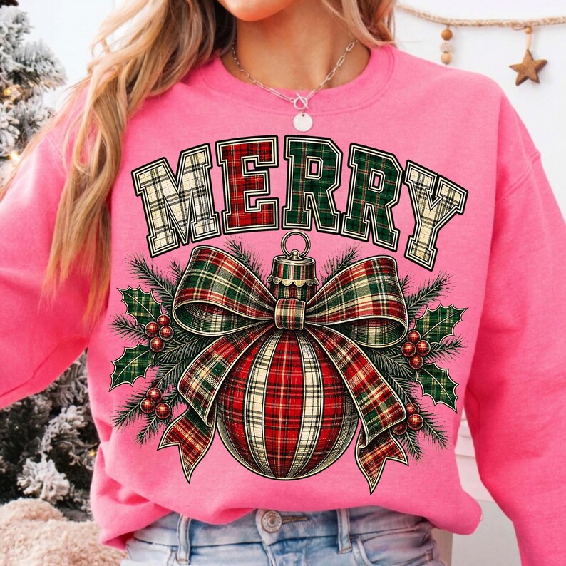 Puede incluir: Una sudadera rosa brillante de manga larga con la palabra MERRY en una fuente de estilo universitario con patr&oacute;n de cuadros. Debajo del texto hay un gr&aacute;fico de un adorno navide&ntilde;o con un lazo de cuadros, ramas de pino verdes y bayas rojas.