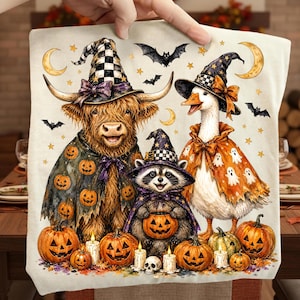 May include: A cream-colored fabric square featuring a printed illustration of a Highland cow, a raccoon, and a goose wearing witch hats and capes. The scene includes jack-o'-lanterns, small ghosts, bats, stars, and crescent moons in orange, black, and white.