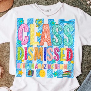 May include: A white t-shirt featuring a colorful graphic with blue diagonal stripes. The text reads "CLASS DISMISSED" and "HAVE AN AMAZING SUMMER" in multi-colored letters. The design includes a globe, ruler, crayons, pencils, stars, and flowers.