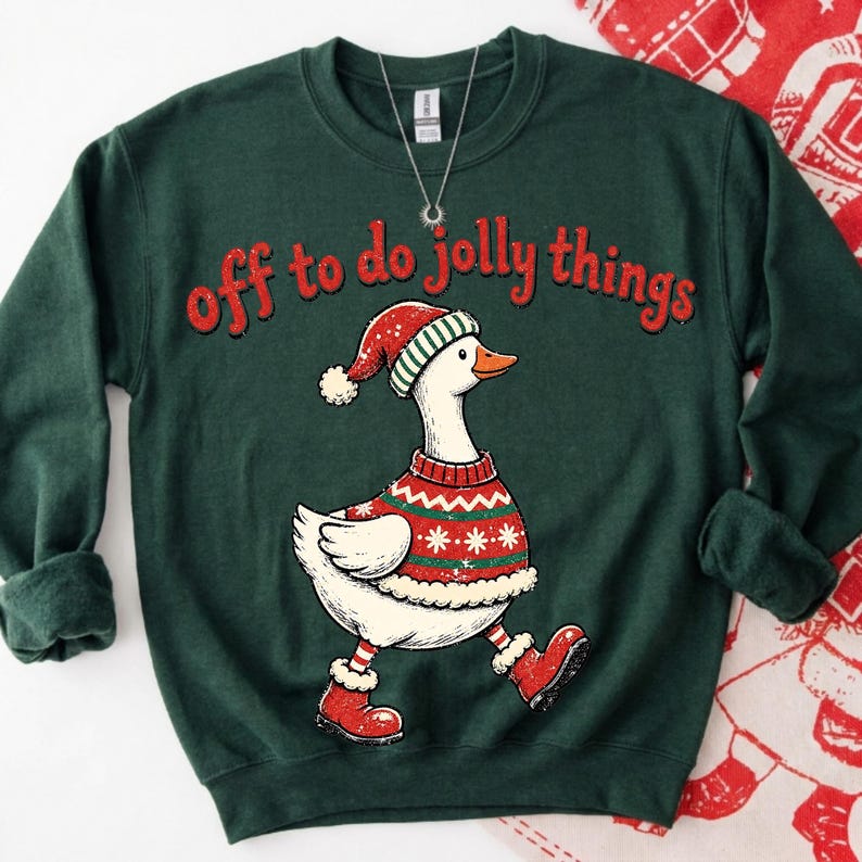 May include: A dark green crewneck sweatshirt featuring a graphic of a white goose wearing a red and green patterned sweater, a matching hat, and red boots. The text "off to do jolly things" is printed in red above the goose illustration.