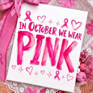 May include: A white rectangular canvas featuring the pink text IN OCTOBER WE WEAR PINK in a brushstroke style. The design includes pink awareness ribbons, hearts, and four-pointed star accents. A pink ribbon bow is attached to the top left corner.