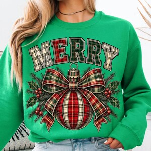 Puede incluir: Una sudadera verde brillante de cuello redondo con la palabra MERRY en fuente de bloque con patr&oacute;n de cuadros. Debajo del texto hay un gr&aacute;fico de un adorno navide&ntilde;o grande con un lazo de cuadros, agujas de pino y bayas rojas, blancas y verdes.