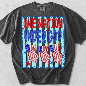 May include: A charcoal gray t-shirt featuring a graphic print with the text ONE NATION UNDER GOD in red and blue. The design includes three American flags hanging on a clothesline against a background of vertical black and light blue stripes.