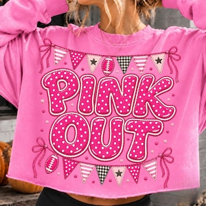 K&ouml;nnte beinhalten: Ein leuchtend pinkfarbenes Langarm-Sweatshirt mit dem Schriftzug PINK OUT in gro&szlig;en, wei&szlig; gepunkteten Buchstaben. Das Design enth&auml;lt dekorative Wimpelketten mit Sternen, Streifen und Karomustern sowie zwei Illustrationen von Footballs.