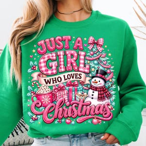 May include: A bright green sweatshirt featuring a graphic print with the text JUST A GIRL WHO LOVES CHRISTMAS. The design includes a decorated Christmas tree, a snowman wearing a plaid scarf, wrapped gifts, and a mug of hot cocoa with a candy cane.