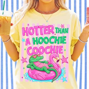 Może przedstawiać: Jasnoż&oacute;łty t-shirt z grafiką przedstawiającą zielonego aligatora w okularach przeciwsłonecznych w kształcie serc, leżącego na r&oacute;żowym kole do pływania w kształcie flaminga. Napis HOTTER THAN A HOOCHIE COOCHIE jest w kolorze r&oacute;żowym i zielonym.