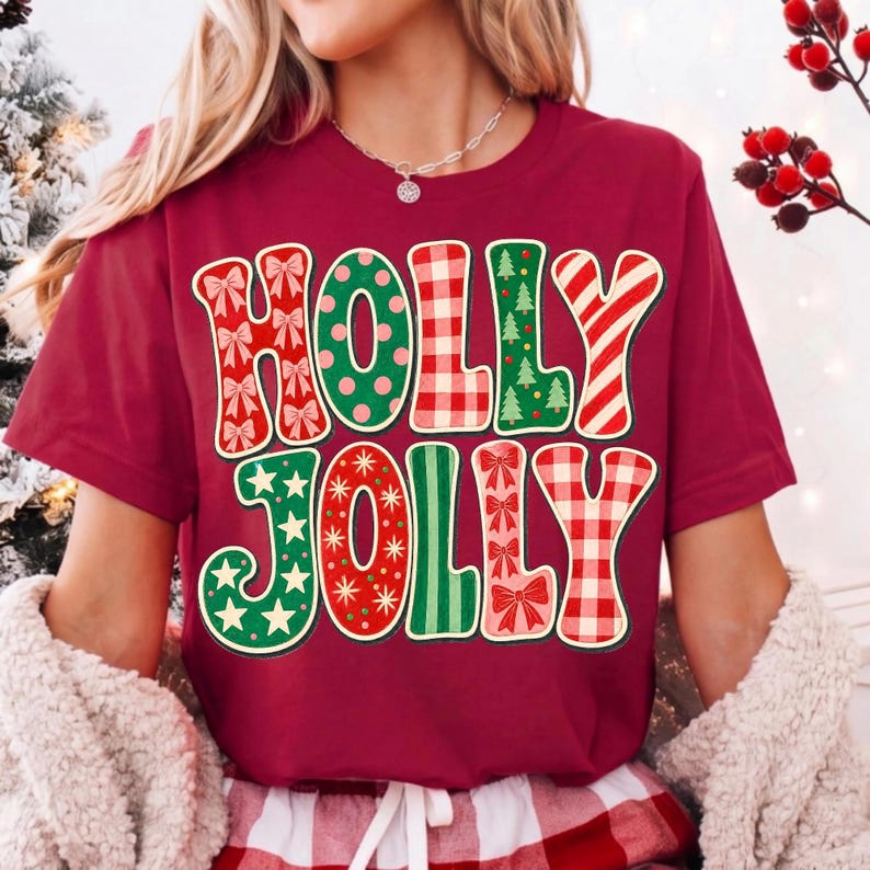 May include: A maroon short-sleeved t-shirt featuring the text HOLLY JOLLY in large, multi-patterned letters. The letters include designs of red bows, green polka dots, red and white gingham, green Christmas trees, and red candy cane stripes.