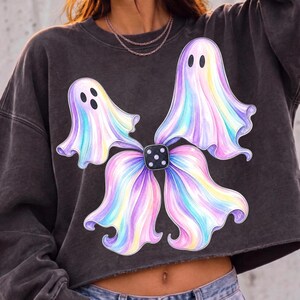 May include: A charcoal grey cropped sweatshirt featuring a graphic print of two pastel-coloured ghosts with iridescent purple, blue, and yellow hues. The ghosts are connected at the centre by a black square die with white pips, forming a bow-like shape.