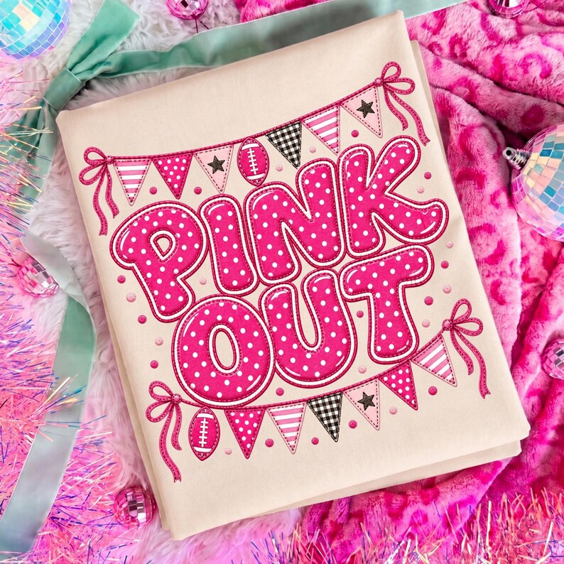 K&ouml;nnte beinhalten: Ein cremefarbenes T-Shirt mit dem Schriftzug "PINK OUT" in gro&szlig;en, kr&auml;ftigen, pinkfarbenen Buchstaben mit wei&szlig;en Punkten. Das Design wird von zwei Reihen Wimpelketten mit Fu&szlig;b&auml;llen, Sternen und Karomustern in Pink und Schwarz eingerahmt.