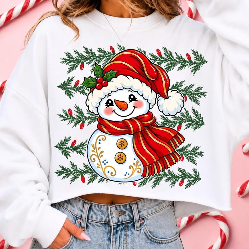 May include: A white cropped sweatshirt featuring a graphic of a snowman wearing a red Santa hat and a red scarf. The snowman has a carrot nose, two gold buttons, and decorative gold swirls. The background print includes green pine branches.