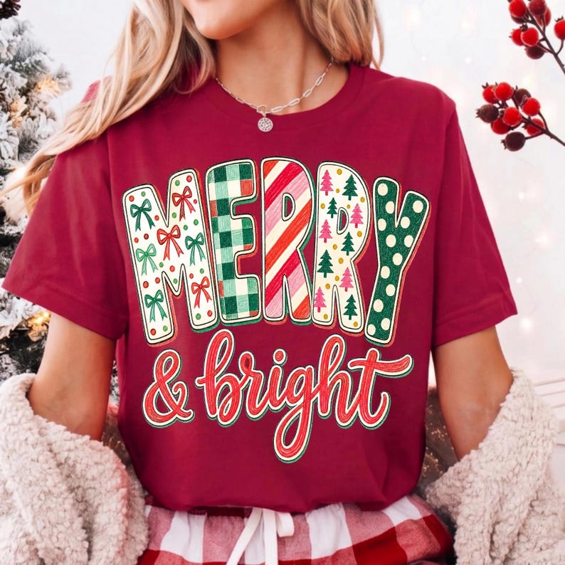 May include: A maroon short-sleeve t-shirt featuring the text MERRY in large block letters with varied patterns including green bows, green plaid, red and white candy cane stripes, small pine trees, and green polka dots, with & bright below.