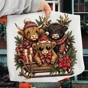 Puede incluir: Una tela blanca con una ilustraci&oacute;n festiva de tres vacas Highland en un trineo de madera. Una vaca lleva un gorro de punto rojo, otra tiene astas de reno y una bufanda, y la tercera lleva gafas de sol y un lazo rojo, entre regalos y ramas.