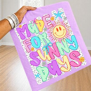 May include: A light purple fabric square featuring the text MADE FOR SUNNY DAYS in colorful, patterned bubble letters. The design includes a yellow smiley face sun, small flowers, blue starfish, and a black and white polka dot background pattern.