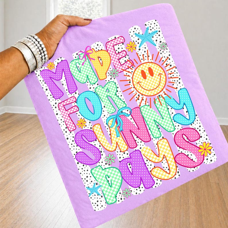 May include: A light purple fabric square featuring the text MADE FOR SUNNY DAYS in colorful, patterned bubble letters. The design includes a yellow smiley face sun, small flowers, blue starfish, and a black and white polka dot background pattern.