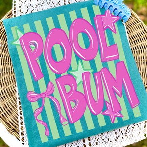 May include: A teal pillow with the words "POOL BUM" in large, bubble-style pink letters. The pillow has green vertical stripes and is decorated with pink stars and a bow. A blue item is visible in the top right corner.