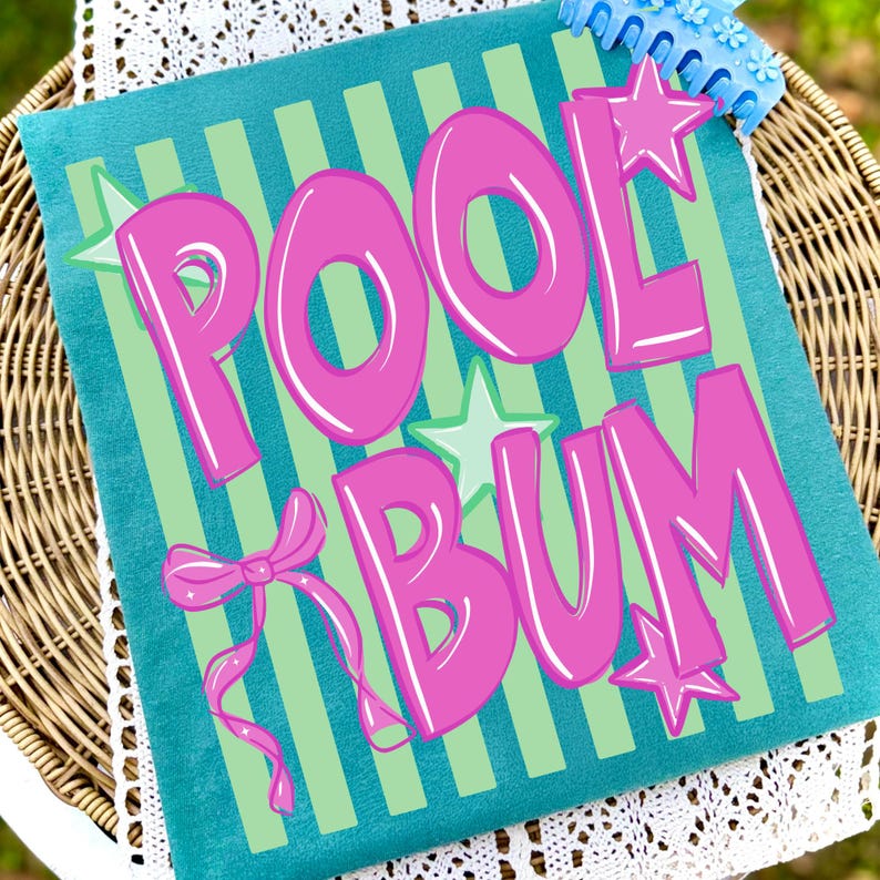 May include: A teal pillow with the words "POOL BUM" in large, bubble-style pink letters. The pillow has green vertical stripes and is decorated with pink stars and a bow. A blue item is visible in the top right corner.
