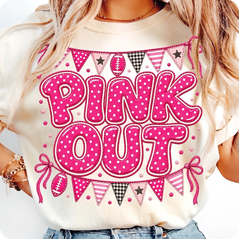 K&ouml;nnte beinhalten: Ein cremefarbenes T-Shirt mit einem Grafikdruck, der den Text PINK OUT in gro&szlig;en, rosa, wei&szlig; gepunkteten Buchstaben zeigt. Das Design umfasst rosa Wimpelketten mit Sternen, Streifen und Footballs, die an den Enden mit rosa Schleifen gebunden sind.