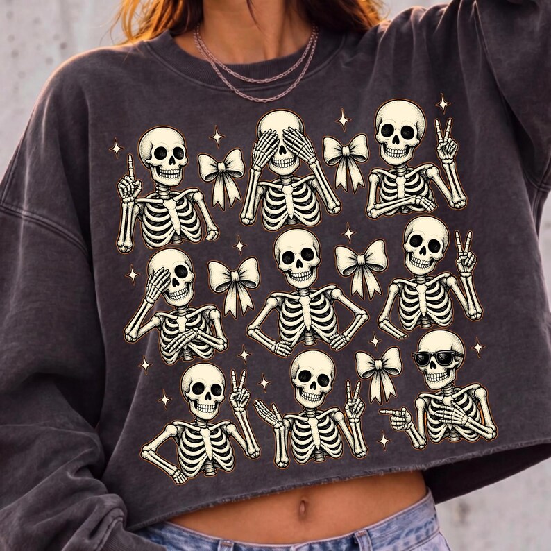 May include: A charcoal gray crewneck sweatshirt featuring a graphic print of nine skeletons in various poses, interspersed with small white bows and four-pointed stars. The skeletons are depicted with different hand gestures, including peace signs and pointing.