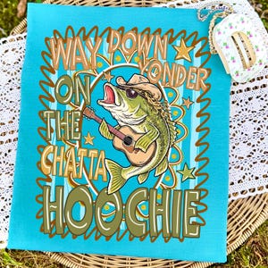 May include: A turquoise blue towel with a graphic of a fish wearing a cowboy hat and sunglasses, playing a guitar. The text on the towel reads "Way Down Yonder On The Chatta Hoochie."
