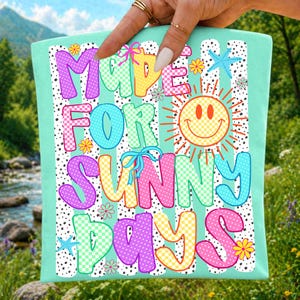 May include: A light mint green fabric square featuring the text MADE FOR SUNNY DAYS in colorful, patterned bubble letters. The design includes a yellow smiley face, small blue starfish, and tiny flowers over a background of vertical black dotted stripes.